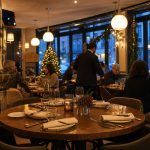 Salle de restaurant française chaleureuse et élégante ouverte le jour de Noël, avec tables dressées, lumière ambrée et décorations hivernales discrètes.