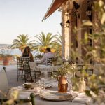 Terrasse de restaurant méditerranéen à Hyères au coucher du soleil, avec tables dressées, palmiers et vue sur la mer