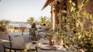 Terrasse de restaurant méditerranéen à Hyères au coucher du soleil, avec tables dressées, palmiers et vue sur la mer