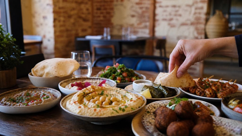 Table généreuse de mezzés libanais dans un restaurant chaleureux à Lille, avec houmous, falafels, pain pita, feuilles de vigne et brochettes grillées.