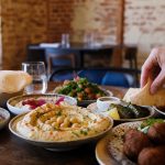 Table généreuse de mezzés libanais dans un restaurant chaleureux à Lille, avec houmous, falafels, pain pita, feuilles de vigne et brochettes grillées.