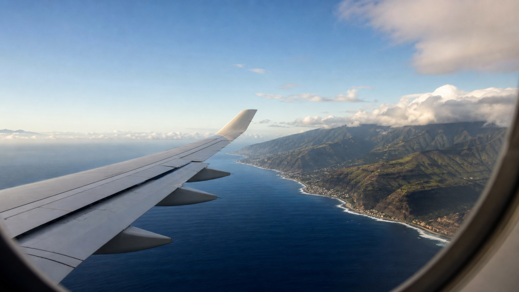 Vue depuis un avion en approche de La Réunion, avec une aile au premier plan, l’océan Indien et les reliefs volcaniques de l’île.