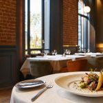 Restaurant gastronomique élégant à Lille avec plat raffiné, tables nappées et murs de briques chaleureuses.