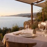 Terrasse de restaurant méditerranéen au Lavandou au coucher du soleil, avec table élégamment dressée face à la mer.